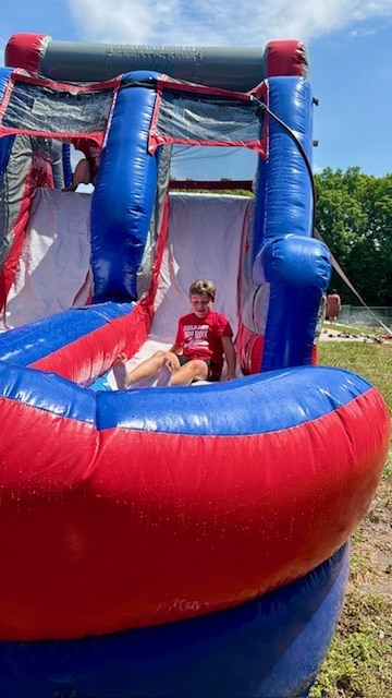 A child wearing a red shirt slides down an inflatable water slide, which is blue and red.