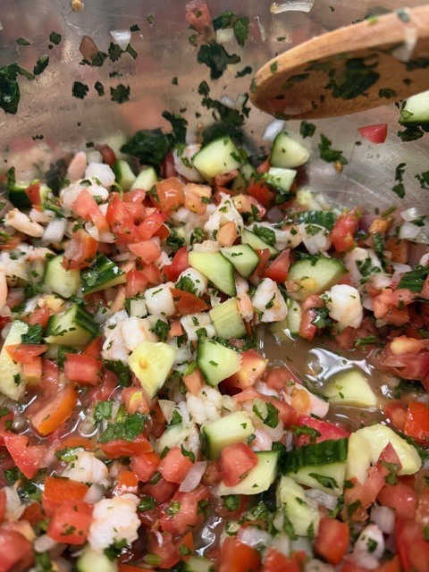 Salad with shrimp, chopped tomatoes, cucumbers, and cilantro in a bowl, mixed with a wooden spoon.