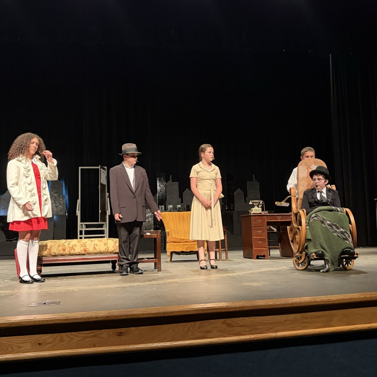 Four students in Annie attire on stage. One student in wheelchair in period costume  