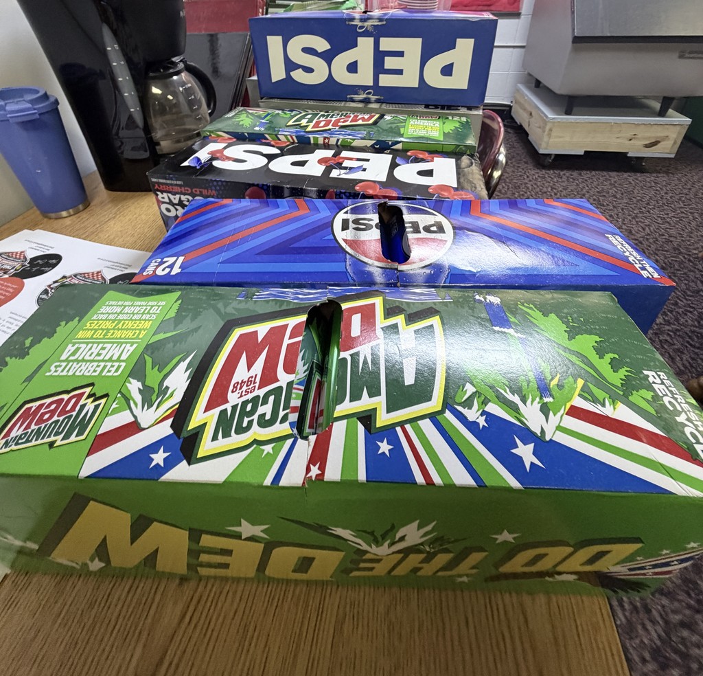 Three Mountain Dew boxes stacked on a table. One box is upside down, and another has a missing lid.
