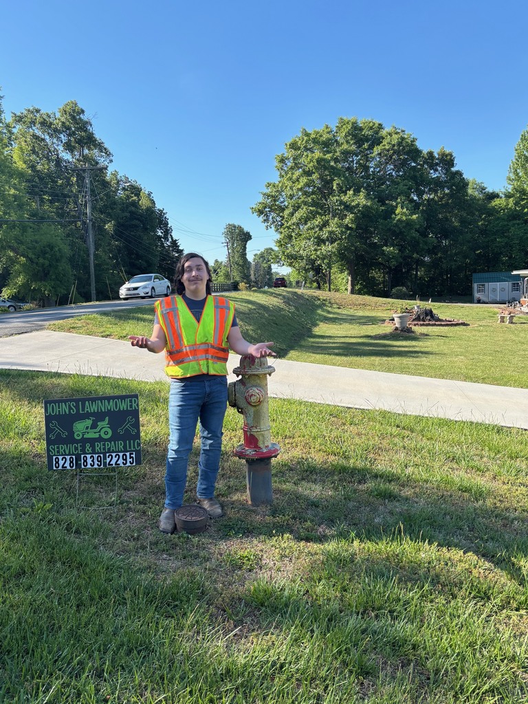 Person wearing a neon yellow vest stands next to a decorative hydrant on a grassy field.