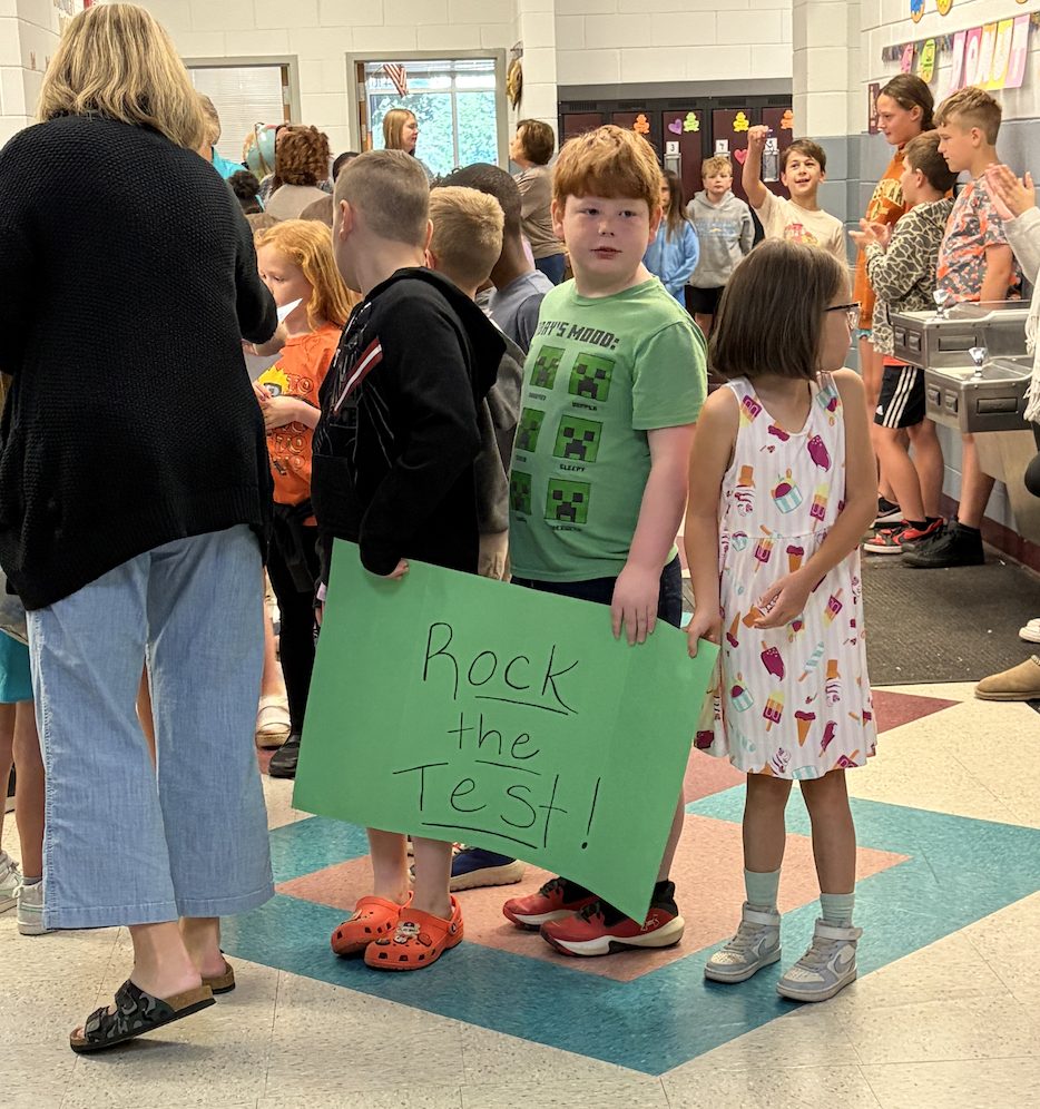 Group of children holding a sign that reads "Rock the Test!" standing in a school hallway.