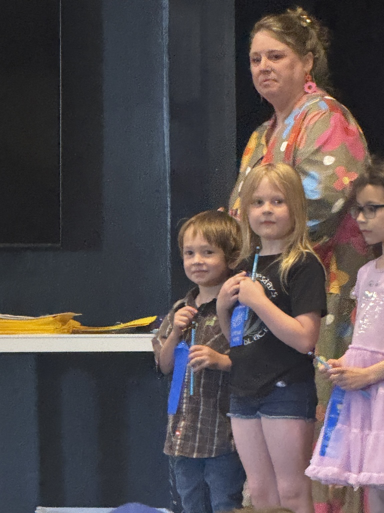 Three children and an adult standing together. One woman wears a colorful dress. The children wear medals.