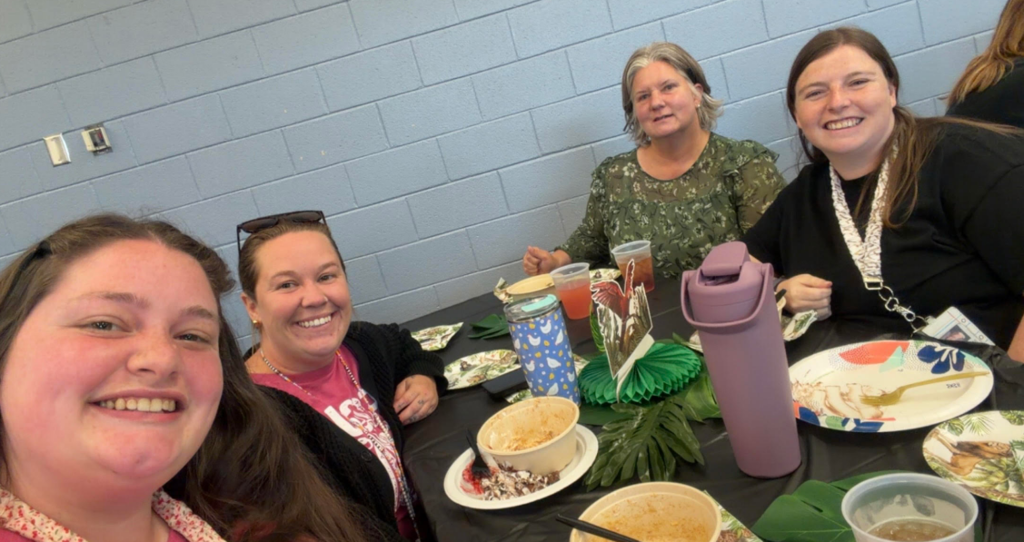 Four people seated around a table, smiling and posing for a photo with various dishes and drinks.
