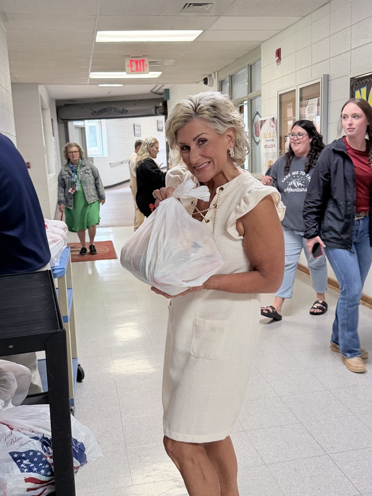 A woman in a white dress holds a bag of groceries in a brightly lit hallway.
