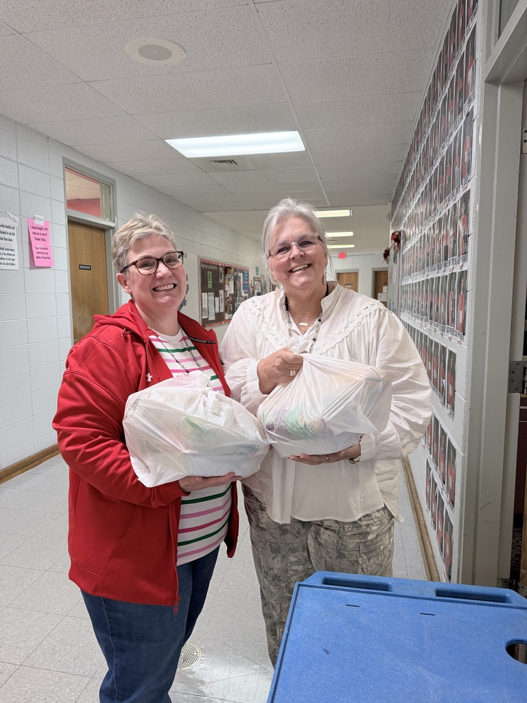 Two women in glasses hold white bags, one in a red jacket and the other in a white top.