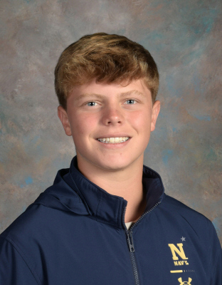A person in a navy blue jacket with "NAVY" and an Under Armour logo, smiling and looking at the camera.