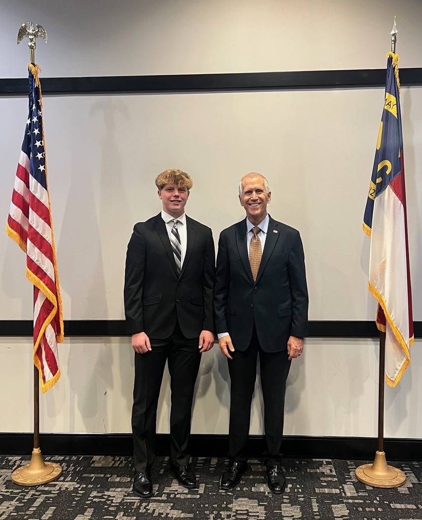 Two men in suits stand between two poles with flags, one showing the US and the other the state of Georgia.