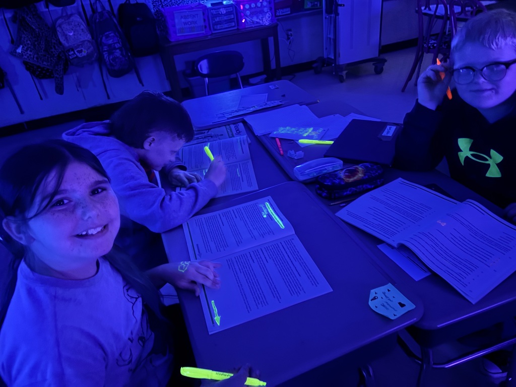 Three children sit at a table with glowing markers, one smiling and two focused on papers.