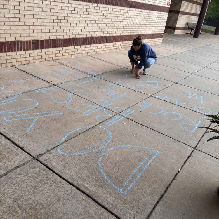 picture of the front of a school with chalk on the sidewalk saying “do your best, you’ve got this, rock this EOG we love you