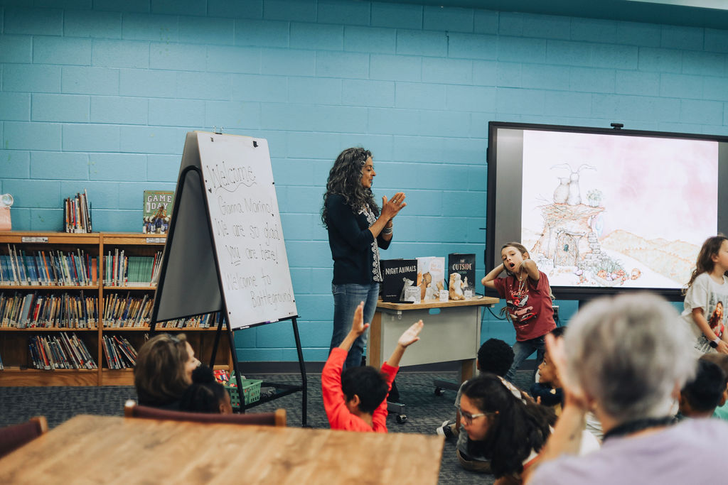 An instructor stands by a screen and whiteboard, addressing a group of students in a classroom setting.