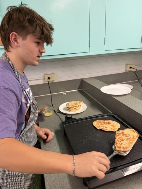 Person in an apron uses a spatula to lift cooked food from a griddle to a plate.