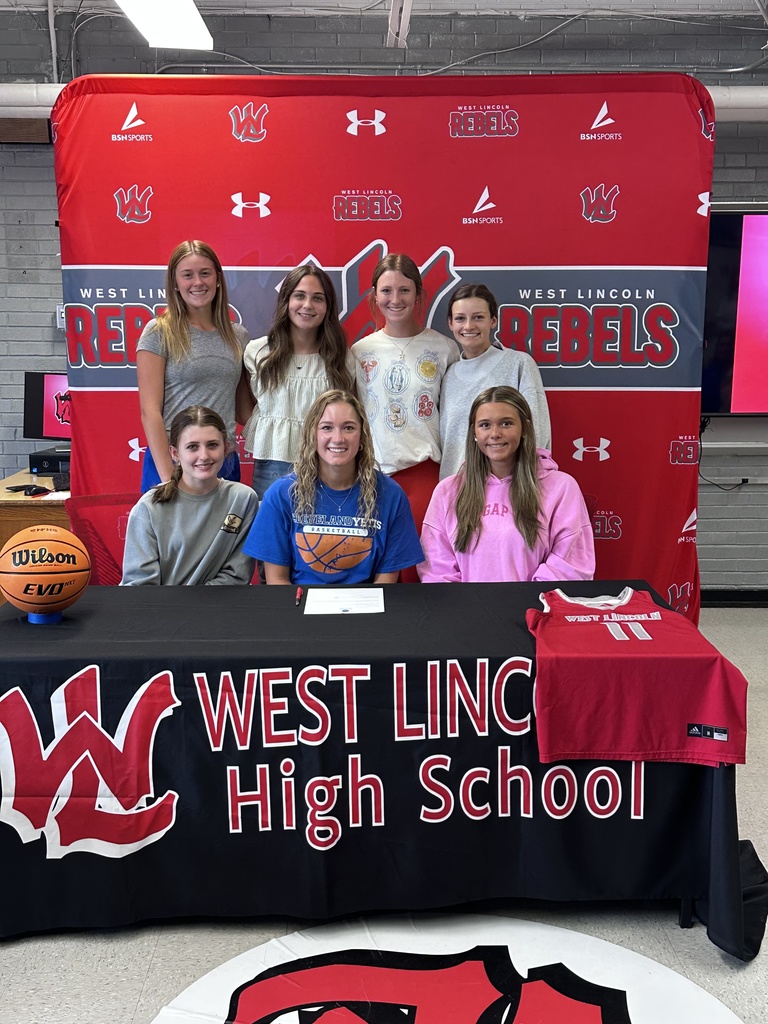 Six girls stand behind a table, smiling. A red banner behind them reads "WEST LINCOLN REBELS" in white. The table has a black cloth and displays "WEST LINC High School".