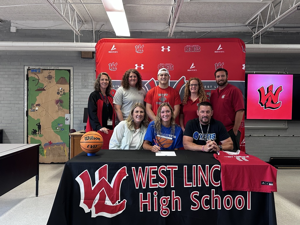 A group of people stands behind a table, signing. The table has a West Lincoln High School banner.