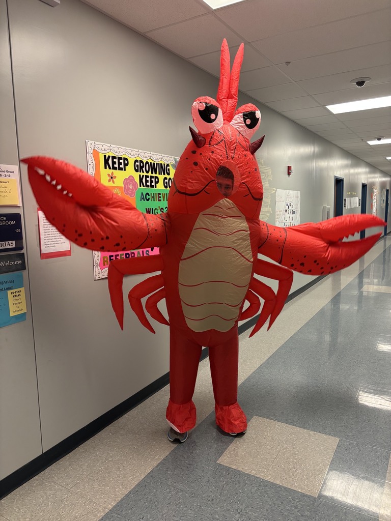 A person dressed as a lobster with large red claws stands in a hallway with tiled flooring and bulletin boards.
