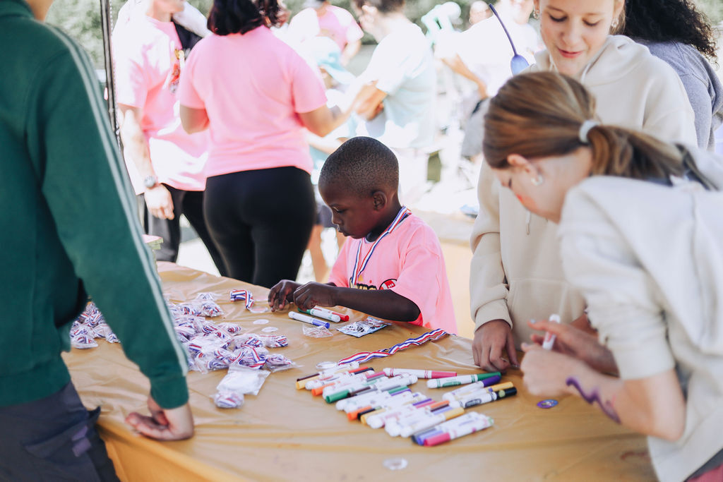 A child in a pink shirt and a few adults at a table, crafting with colorful items.