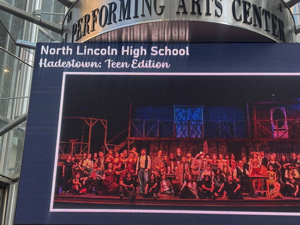 A framed photo of people performing a play, displayed outside North Lincoln High School Performing Arts Center.