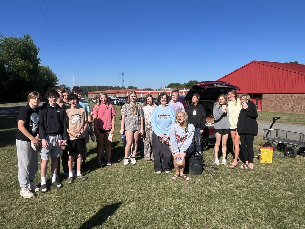 A group of people in various colored clothing pose for a photo in a grassy field.
