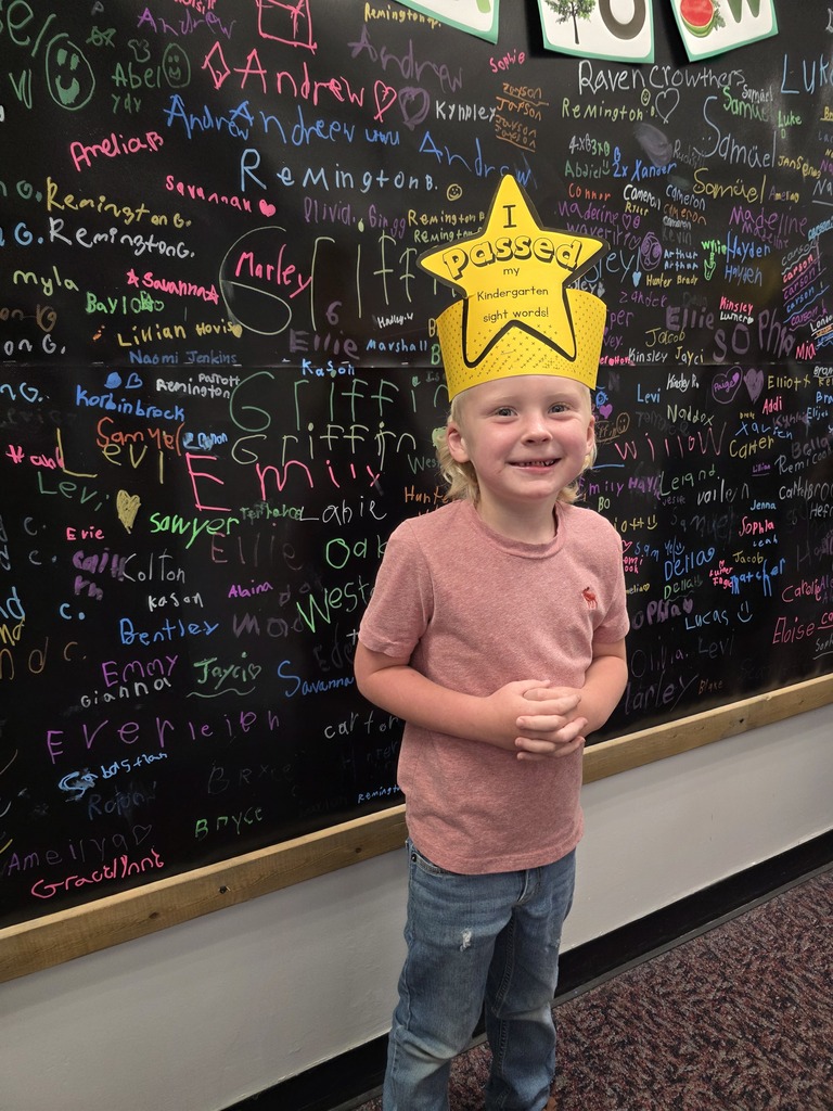 A child wears a yellow star-shaped hat and stands in front of a wall covered in writing.