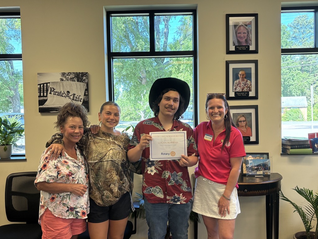 Four adults stand together in an office room, one holding a certificate. Framed photos adorn the wall behind them.