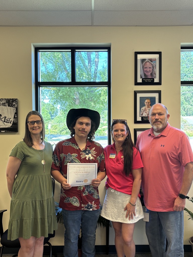 Five people stand in a room with windows and framed pictures on the wall. One person holds a certificate.