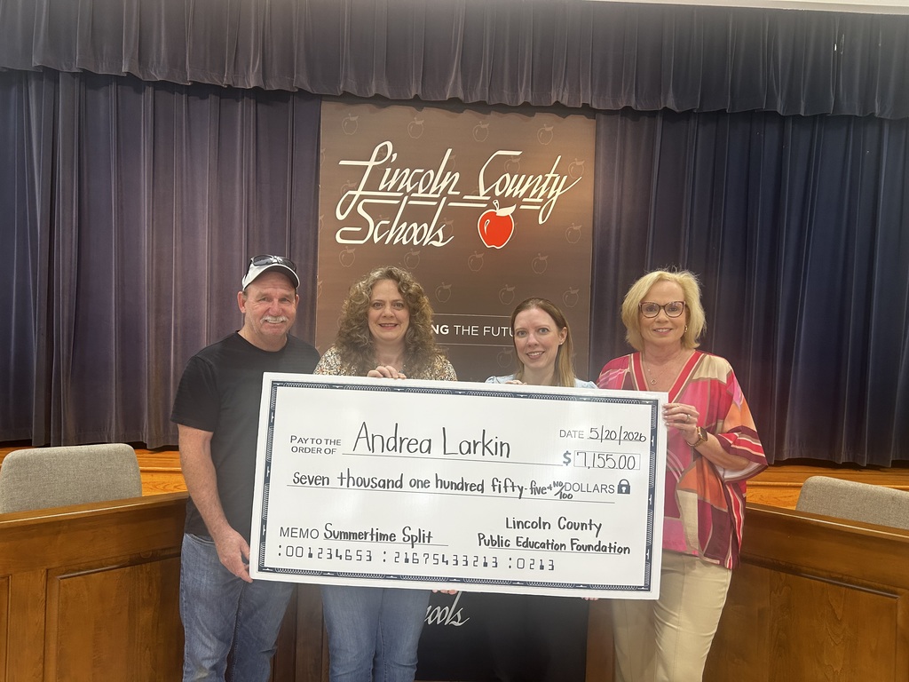 Three people hold a large check in front of a banner that says "Lincoln County Schools."