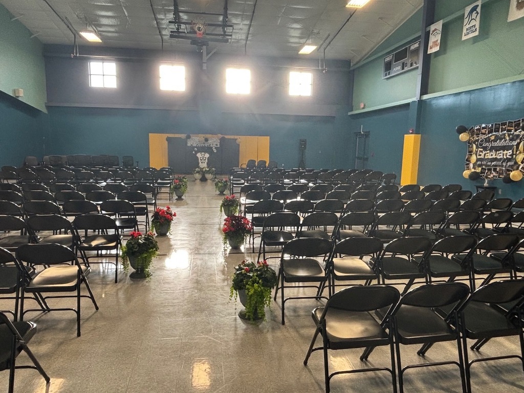 An empty room with rows of black chairs, some with flowers, blue walls, and a yellow pillar.