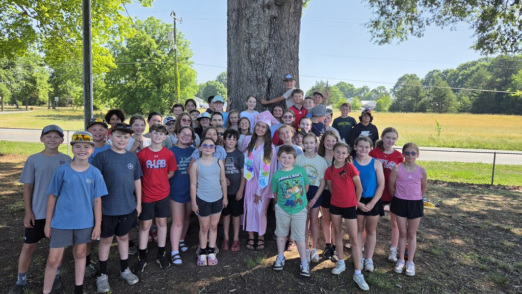 A group of children and adults in sports attire posing under a large tree in a park.