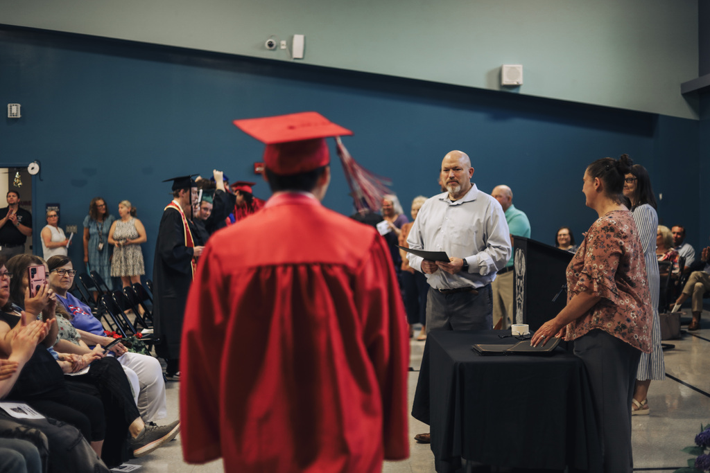 People at a graduation ceremony. A person in a red gown faces away from the crowd.