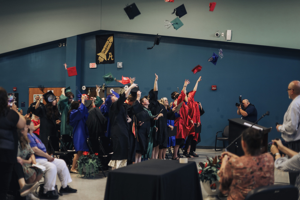 Graduates in gowns and caps throwing their caps in the air during a ceremony.