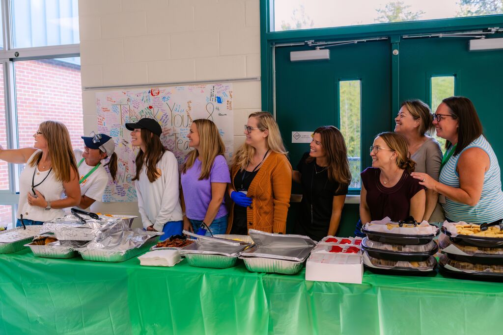 A group of women in a room with a green table covered in food. They look at the table.