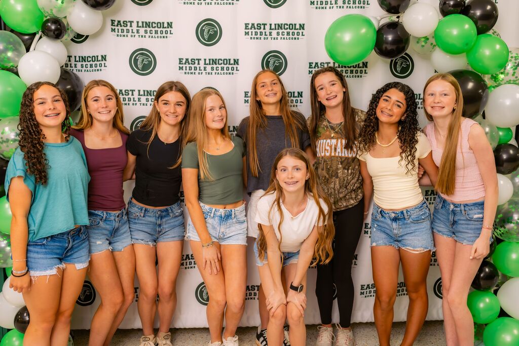 Group of young women in casual clothes standing in front of a colorful balloon arch.