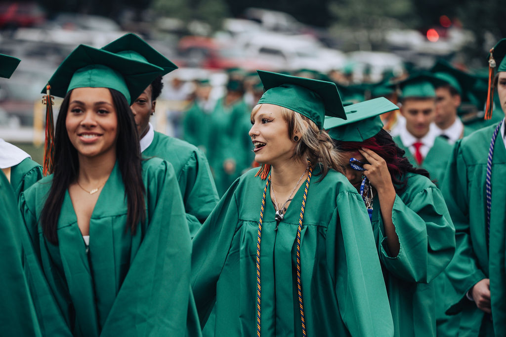 A row of students wearing green caps and gowns, with some smiling and others holding their caps.