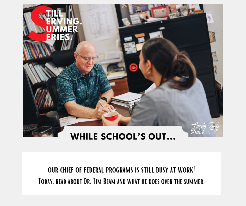An older man and a woman talk at a desk. Behind them is a bookshelf and a file cabinet.