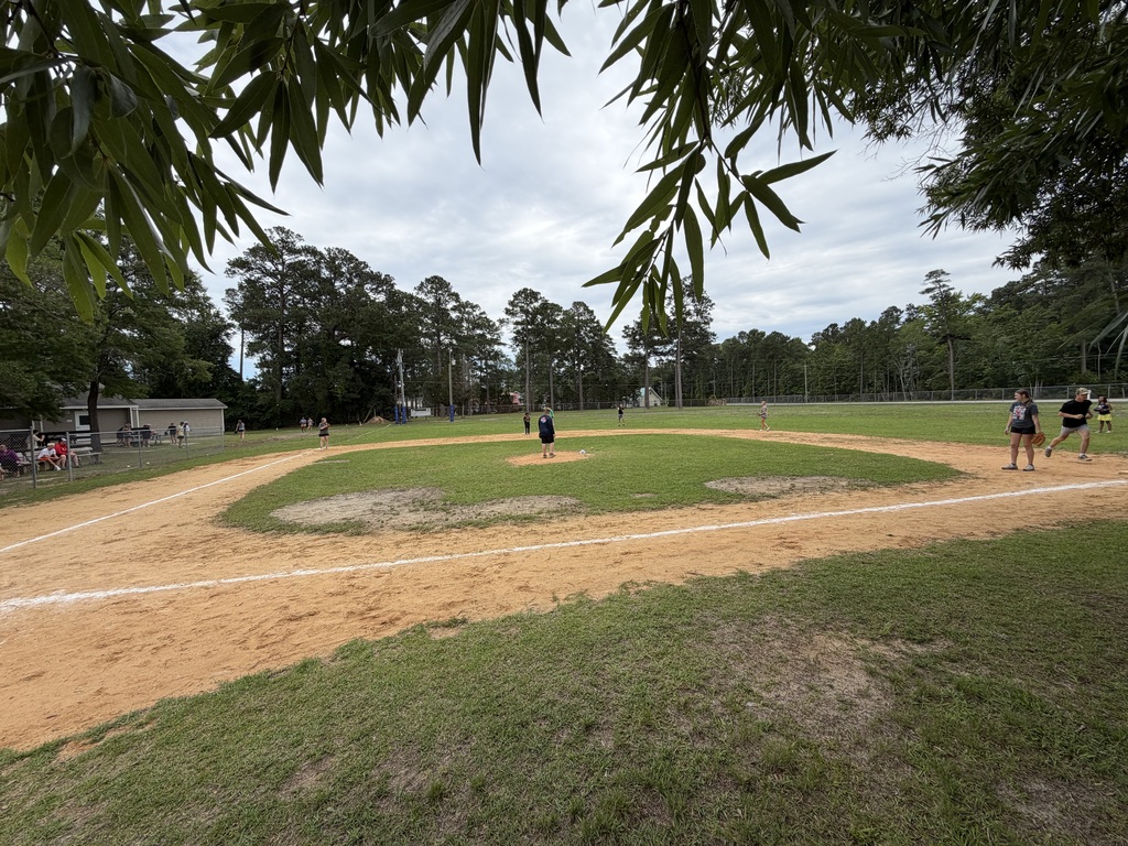 An open baseball field with dirt infield and grassy outfield. People are standing in the distance.