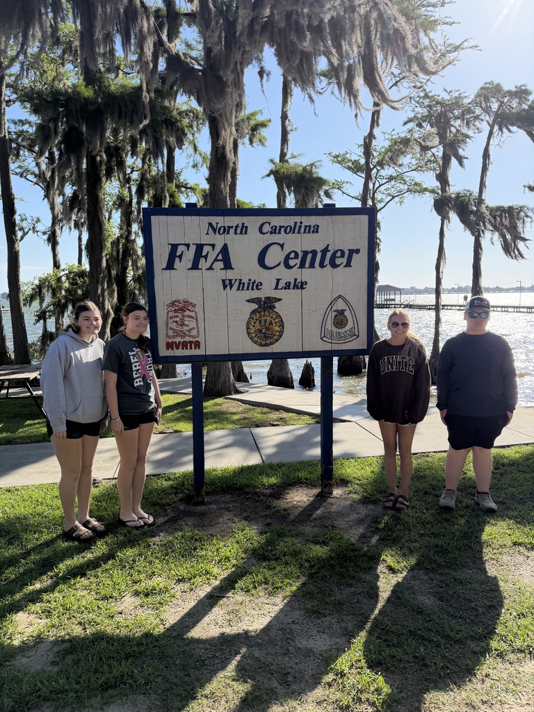 Five people pose in front of a white sign with "FFA Center" text, next to a lake and trees.