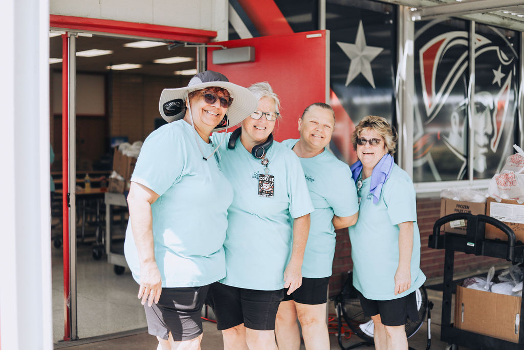 Four women in matching teal shirts and black shorts, standing outside a red door with a star on it.