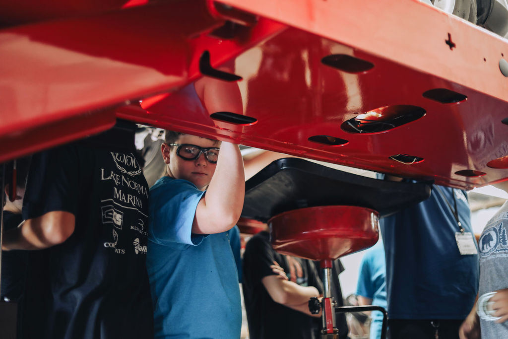 A group of people under a red structure. One person wears glasses and has their hands on the structure.
