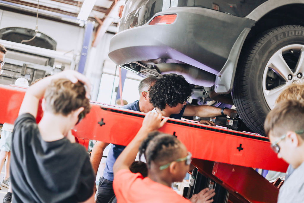 Multiple people working on a vehicle. One person has their head under the car, while others are examining the vehicle.