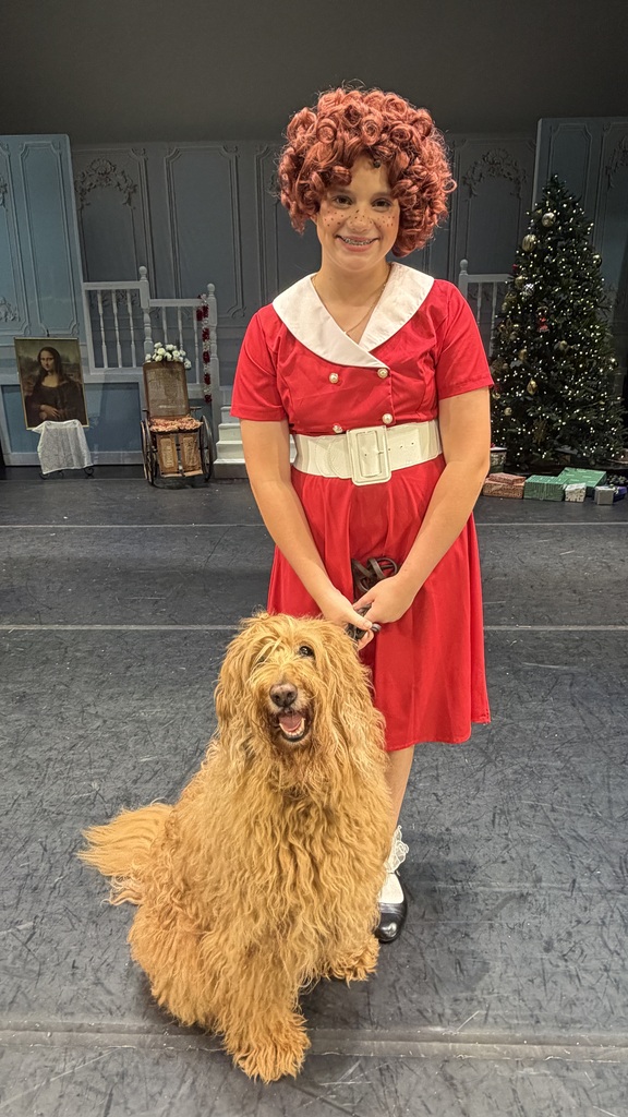 A young girl wearing a red dress with a white collar and belt poses with a dog.