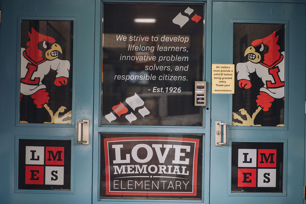 Blue double doors with large decals of a bird. Words on the glass: "We strive to develop lifelong learners, innovative problem solvers, and responsible citizens."
