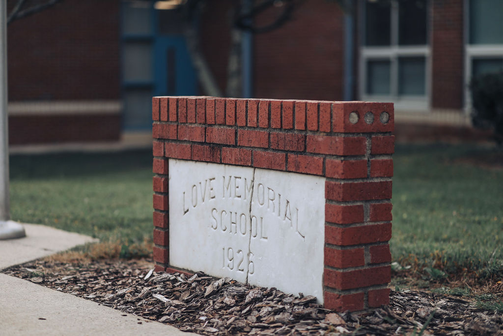 A brick wall with a plaque reading "LOVE MEMORIAL SCHOOL 1924" in front of a building.