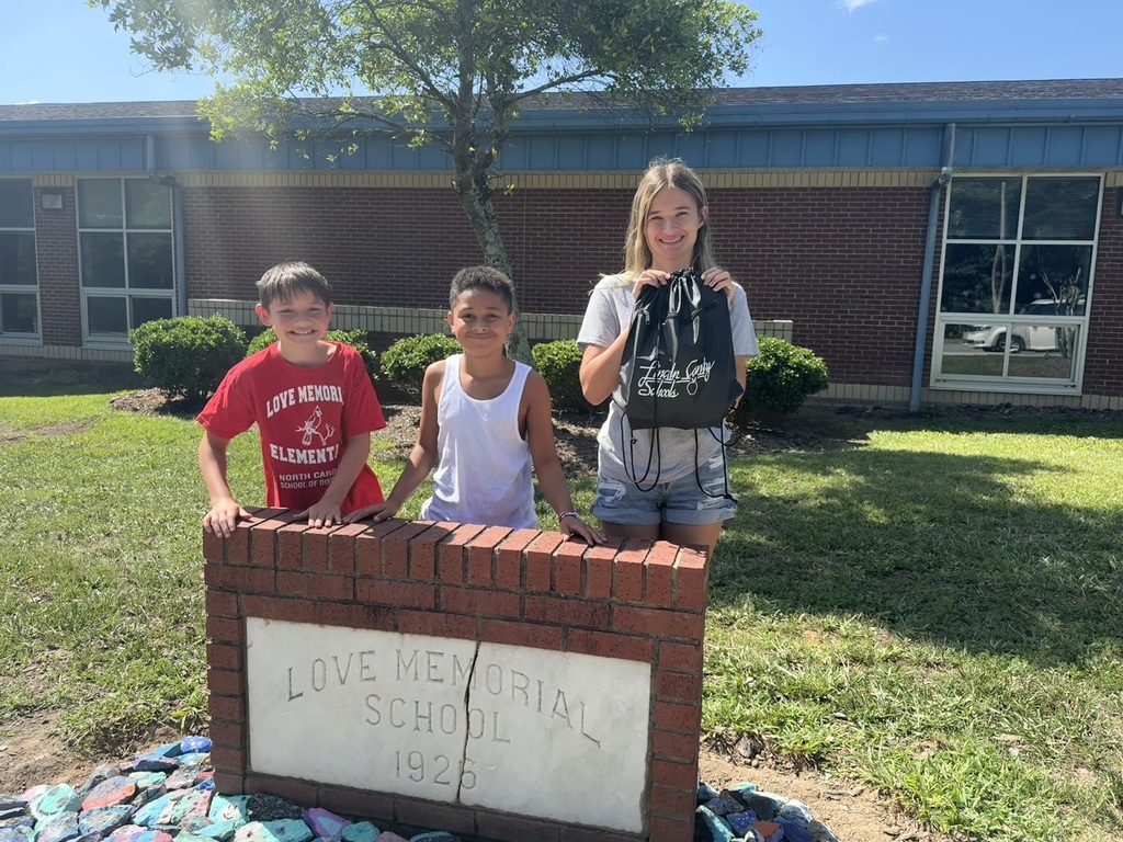 Three children stand by a brick monument reading "LOVE MEMORIAL SCHOOL 1925" in front of a building.