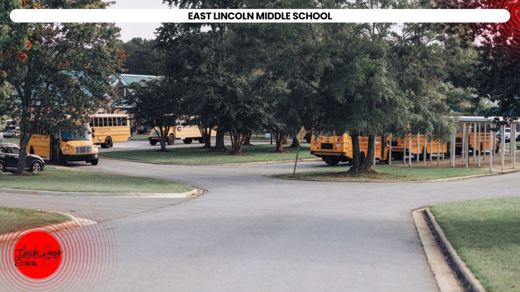 Several yellow school buses parked around trees. The road is empty. Location is East Lincoln Middle School.