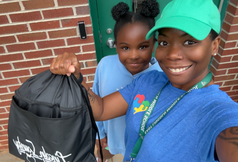 Woman wearing a green hat and blue shirt holding a bag. A girl stands behind her holding a blue bag.