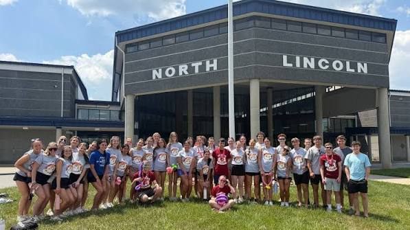 Group of people in white and red T-shirts posing in front of a school building.