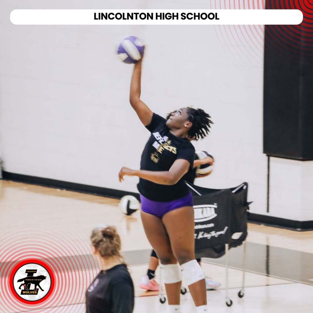 A volleyball player jumps to hit the ball, wearing a black jersey, purple shorts, and white knee pads.