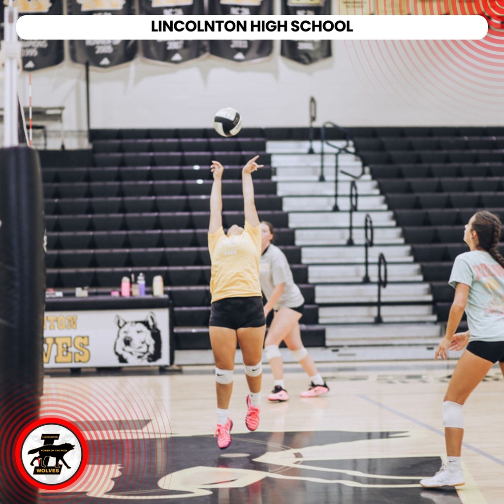 Players in a gym playing volleyball. One player is jumping and hitting the ball over the net.