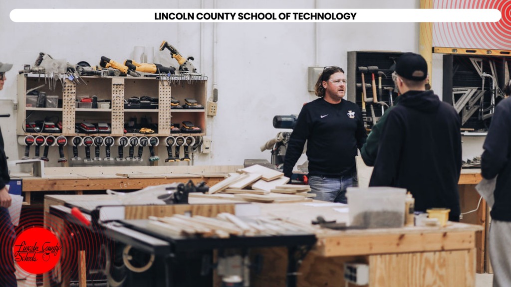 A workshop with a group of people wearing black hoodies. Tools and wood pieces are on the tables.