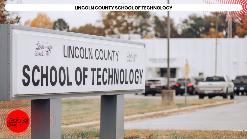 A white sign in front of a grassy area reads "Lincoln County School of Technology" in black. Vehicles parked behind it.